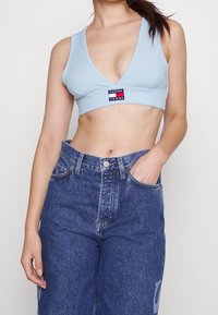 Ljusblå ribbad bralette med djup V-ringning och logopatch, tillsammans med högmidjade mörk denimjeans med en blekt design.