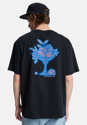 Άνδρας που φοράει μαύρο καπέλο και μαύρο T-shirt με μπλε pixel art φρουτιέρα και λογότυπο Quiksilver στο πίσω μέρος.