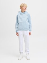 Svetlo modra jopa s kapuco in žepom kenguru, kombinirana s sivimi trenirkami in belimi supergami. Mehka tkanina, sproščen kroj, minimalni detajli blagovne znamke.