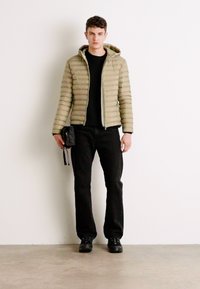 Bežna podložena jakna s vodoravnimi črtami, z zadrgo in kapuco, kombinirana s črnimi hlačami in črnimi čevlji. Model drži majhno črno torbico.