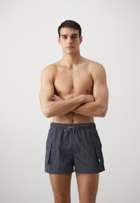 Costumi da bagno da uomo grigio scuro in tessuto leggero. Presentano una vita elasticizzata con cordoncino e due tasche cargo laterali.