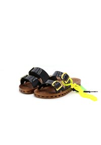 Zwarte glanzende sandalen met twee brede banden, gouden gespen en een bruine gestructureerde zool. Neon gele kwastdetail eraan bevestigd.