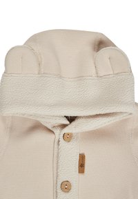 Cream-colored baby hooded sweater with a textured fleece lining, wooden buttons, and rounded ears on the hood. Soft, ribbed fabric.