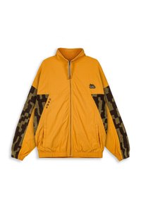 Chaqueta amarilla con cremallera y cuello alto, con mangas de patrón de camuflaje marrón, bolsillos laterales y un pequeño logo en el pecho. Tejido texturizado.