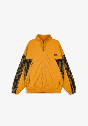 Gele zip-up jas met hoge kraag, voorzien van mouwen met een bruin camouflagepatroon, zijzakken en een klein logo op de borst. Gestructureerde stof.