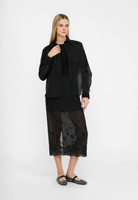 Črno večplastno oblačilo z prosojno srajčo s gumbi in črno podmajico, združeno z krilom srednje dolžine z rožnim vezenjem.