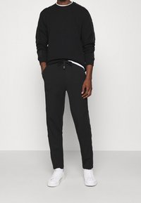 Černá mikina s kulatým výstřihem, se světlým lemem, v kombinaci s černými tepláky s nastavitelným pasem, doplněná o bílé tenisky.