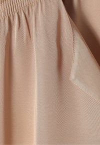 Tessuto beige con una texture liscia presenta un elastico in vita e un dettaglio della tasca laterale. Il design è semplice e funzionale.
