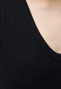 Κοντινό πλάνο ενός ατόμου που φοράει μαύρο ριμπ ζιβάγκο με V-λαιμόκοψη, που δείχνει το λαιμό και το πάνω μέρος του στήθους.