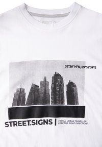 Valkoinen puuvillatee-paita, jossa on mustavalkoinen grafiikka pilvenpiirtäjistä koordinaattien yllä ja teksti "STREET.SIGNS" alapuolella.