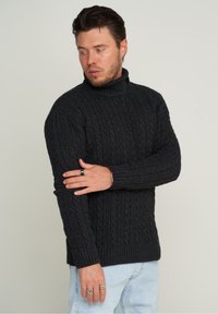 Dunkelgrauer Kabelstrick-Pullover mit Rollkragen, ausgestattet mit gerippten Bündchen und Saum, getragen über hellblauen Jeans. Glattes, strukturiertes Material.