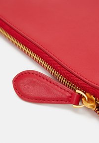 Pochette zippée en cuir rouge avec une fermeture éclair et un tirant dorés, texture lisse et un design simple mettant l'accent sur la fonctionnalité.