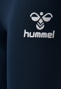 Mörkblå träningstights med en slät yta; har en framträdande vit logotyp och design detaljer på vänster ben.