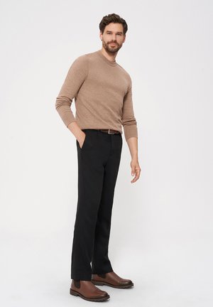 Brązowy sweter wełniany z okrągłym dekoltem, w zestawieniu z czarnymi spodniami i brązowymi skórzanymi botkami do kostki. Tło jest jednolite, białe.