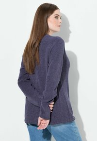 Lila Strickpullover mit langen Ärmeln, strukturiertem Stoff und seitlichen Schlitzen. Kombiniert mit hellblauen Jeans, aus seitlicher Perspektive dargestellt.