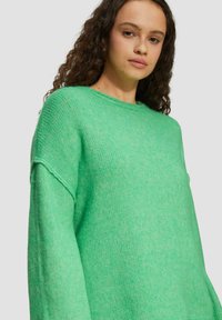 Grüner gestrickter Pullover mit lockerer Passform, weiten Ärmeln und Rundhalsausschnitt. Der Stoff wirkt weich mit einer strukturierten Optik.
