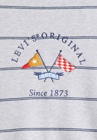 Tissu en coton gris avec des rayures horizontales marines. Présente un logo brodé avec deux drapeaux et le texte "LEVI'S® ORIGINAL" au-dessus et "Depuis 1873" en dessous.