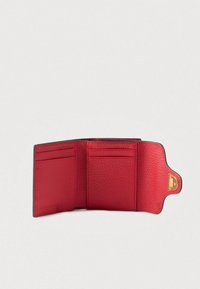 Červená texturovaná kožená peněženka otevřená, aby ukázala více slotů na karty a zlatý klip na neutrálním pozadí.