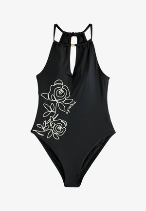 Femeie purtând un costum de baie negru întreg cu model floral alb, stând lângă o piscină cu margine de piatră, aranjându-și părul cu ochii închiși.