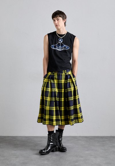 Schwarzes ärmelloses Shirt mit einem blauen grafischen Design, kombiniert mit einem knielangen gelb-blauen karierten Kilt und glänzenden schwarzen Knöchelstiefeln.