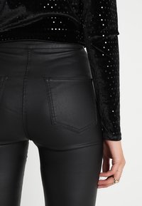 Zwarte aansluitende faux leren broek met een hoge taille, voorzien van achterzakken en een gladde textuur, gecombineerd met een langemouwen top met een glinsterend patroon.