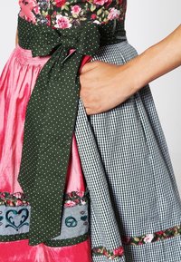 Traditioneel kleed met een bloemige lijfje, roze satijnen rok, groene schort met stippen en strik, en een gingham patroon. Inclusief geborduurde accenten.