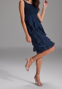 Vestido de gasa navy con volantes en capas, diseño sin mangas y corpiño ajustado; combinado con tacones altos plateados con tiras.