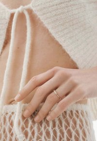 Anillo delicado de oro con una gema ovalada, colocado sobre una suave y difusa tela de punto blanca con una textura de encaje.
