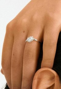 Zilveren ring met een madeliefjes bloem ontwerp, met complexe bloemblad details en een centrale edelsteen, gedragen op een hand met een natuurlijke huidskleur.