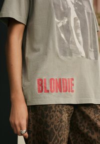 Grå bomulds t-shirt med et sort-hvidt grafisk print og fed rød "BLONDIE" tekst forneden, parret med leopardprintbukser.