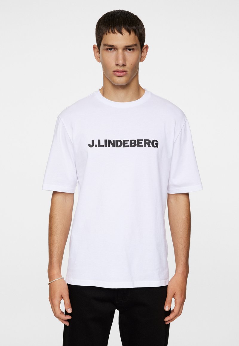 Valge puuvillane T-särk lühikeste varrukatega, millel on must "J. LINDEBERG" tekst rinna kohal. Klassikaline ümar kaelus, mugav lõige.