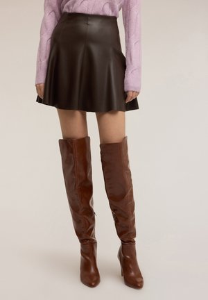 Gonna marrone in pelle a linea A, tessuto testurizzato, abbinata a stivali marroni al ginocchio e a un maglione lavorato a trecce viola chiaro.