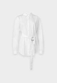 Camicia bianca con maniche lunghe, vita stretto in vita con un anello di metallo, vestibilità sagomata e tessuto di cotone liscio.