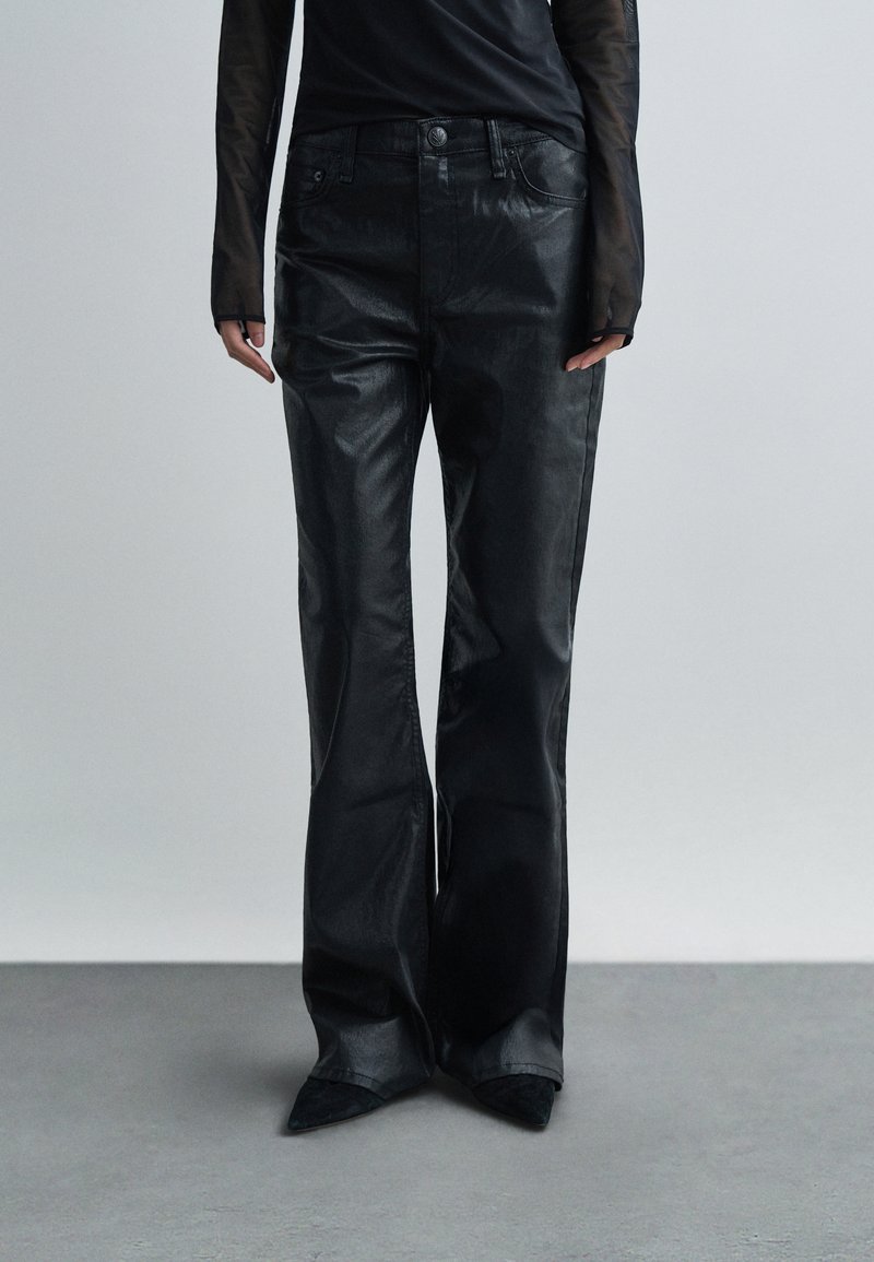 Čierne zvonové nohavice z lesklého, textúrovaného materiálu. Sú vybavené prednými vreckami a priliehavým pásom, doplnené o špicaté čierne topánky.