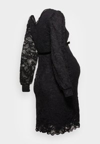 Melna mežģīņu kleita ar garām piedurknēm, ar pieguļošu jostasvietu un viļņotu apakšmalu. Auduma faktūra ir sarežģīta, ar ziedu rakstiem visā kleitā.