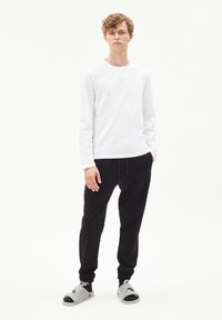 Witte langemouwen shirt, zwarte jogger pants en grijze instap sandaal. Heeft een relaxte pasvorm en casual ontwerp.