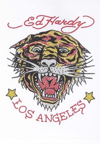 Grafika tygra vyrobená z barevných kamínků na bílém pozadí s červeným nápisem "Ed Hardy" a "Los Angeles."