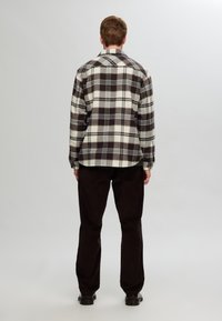 Plaid flannel shirt in cream, brown, and navy; features a traditional collar, button cuffs, and a relaxed fit, paired with black trousers.