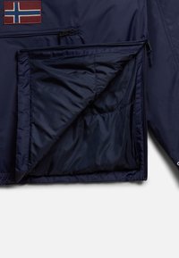 Marinblå bomberjacka med ett röd- och blått Norge-flaggmärke. Har en ficka med dragkedja och vadderad foder. Slätt, lätt material.