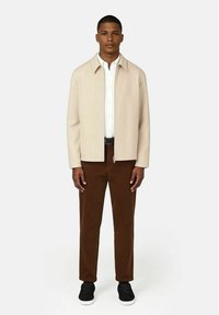 Beige jacka med krage, dragkedjestängning, vit skjorta under, bruna kordbyxor och svarta sneakers. Enkelt, modernt design.