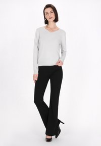 Hellgrauer langärmeliger V-Ausschnitt-Pullover, kombiniert mit schwarzen Schlaghosen, Model in schwarzen High Heels, glatte Texturen, minimalistisches Design.