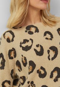 Beige gebreide trui met een luipaardprint in zwarte en bruine tinten, met een zachte textuur en een wijde halslijn.