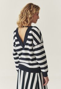 Felpa a righe in cotone navy e bianco con scollatura a V profonda, dotata di maniche ampie e polsini a coste, abbinata a una gonna a righe coordinata.