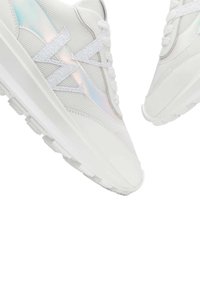 Baskets de sport blanches avec une tige en maille texturée, des accents irisés et des lacets blancs plats, dotées d'une semelle extérieure épaisse pour un meilleur amorti.