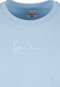 Light blue cotton t-shirt featuring a crew neck, medium size, with white embroidered branding on the front. Smooth texture, casual design.