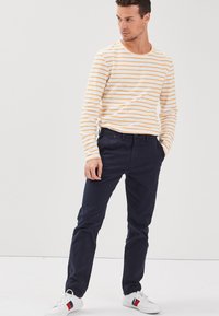 Vit långärmad skjorta med gula horisontella ränder, kombinerad med marinblå chinos och vita sneakers med röda och blå detaljer.