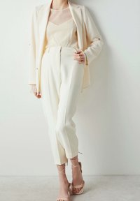 Biała, dopasowana marynarka na teksturowanym kość słoniowa topie, zestawiona z dopasowanymi białymi spodniami i beżowymi sandałkami na cienkich paskach. Minimalistyczny i elegancki design.