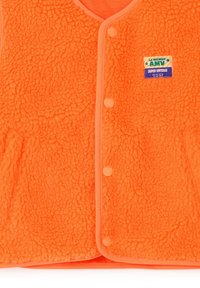 Särav oranž fliisjakk neetidega ja väikese ristkülikukujulise "La Maison Amy Super Vintage" plaastriga rinnal.