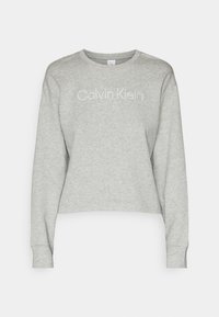 Šedá croppovaná mikina vyrobená z měkké tkaniny. Má dlouhé rukávy a kulatý výstřih s logem "Calvin Klein" v bílé barvě.