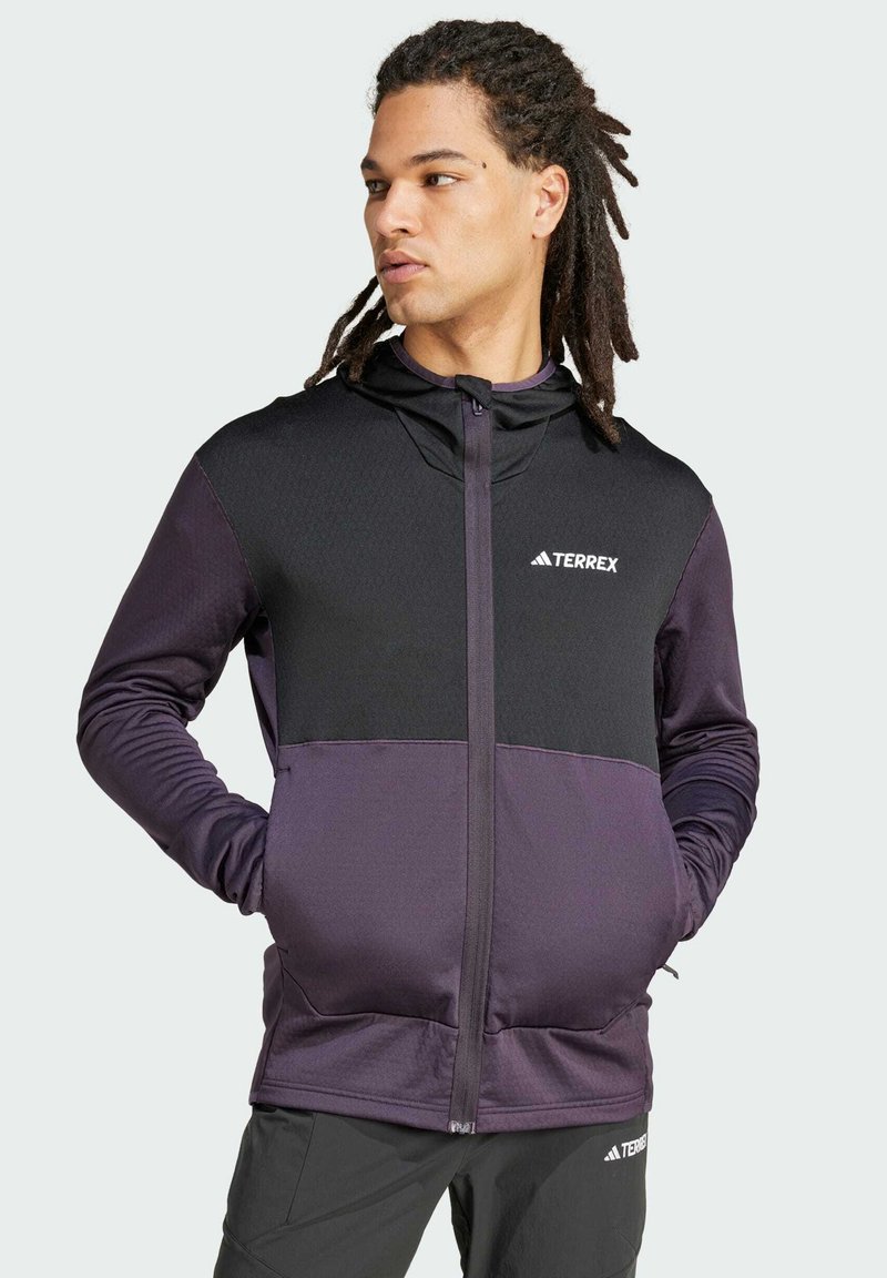 Giacca Terrex nera e viola con zip frontale, cappuccio, pannello superiore texturizzato, pannello inferiore liscio e logo sul petto.